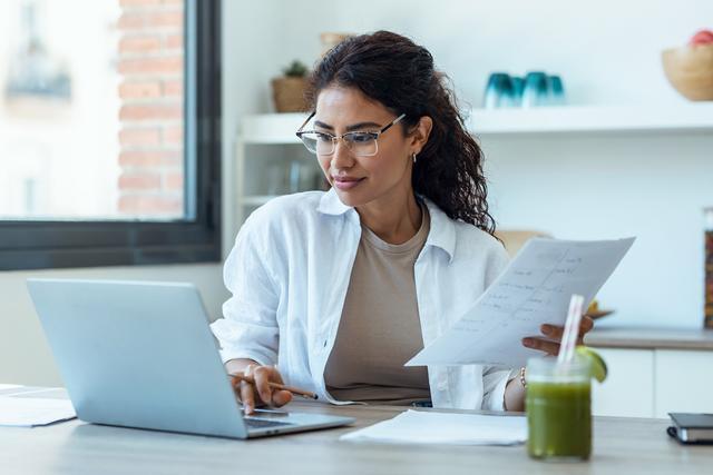 female-latin-american-adult-doctor-consultation-room-working-on-laptop-while-holding-documents-web-1
